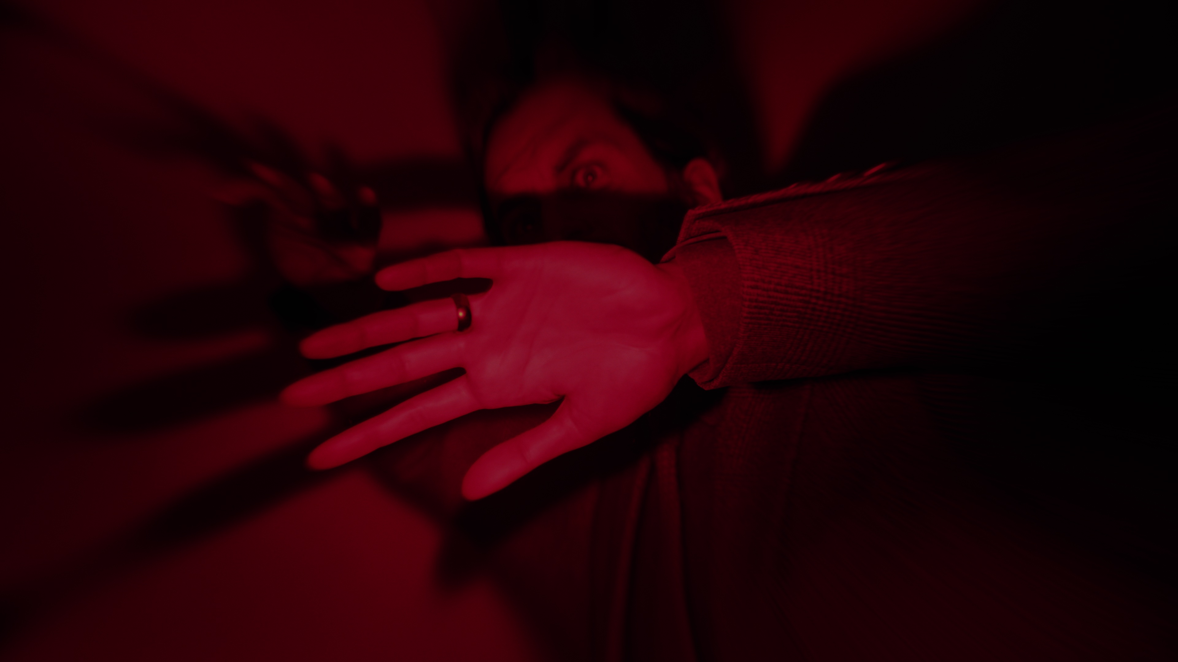 Screenshot ze hry Alan Wake 2 ukazující Alana uvězněného na temném místě pod červeným světlem
