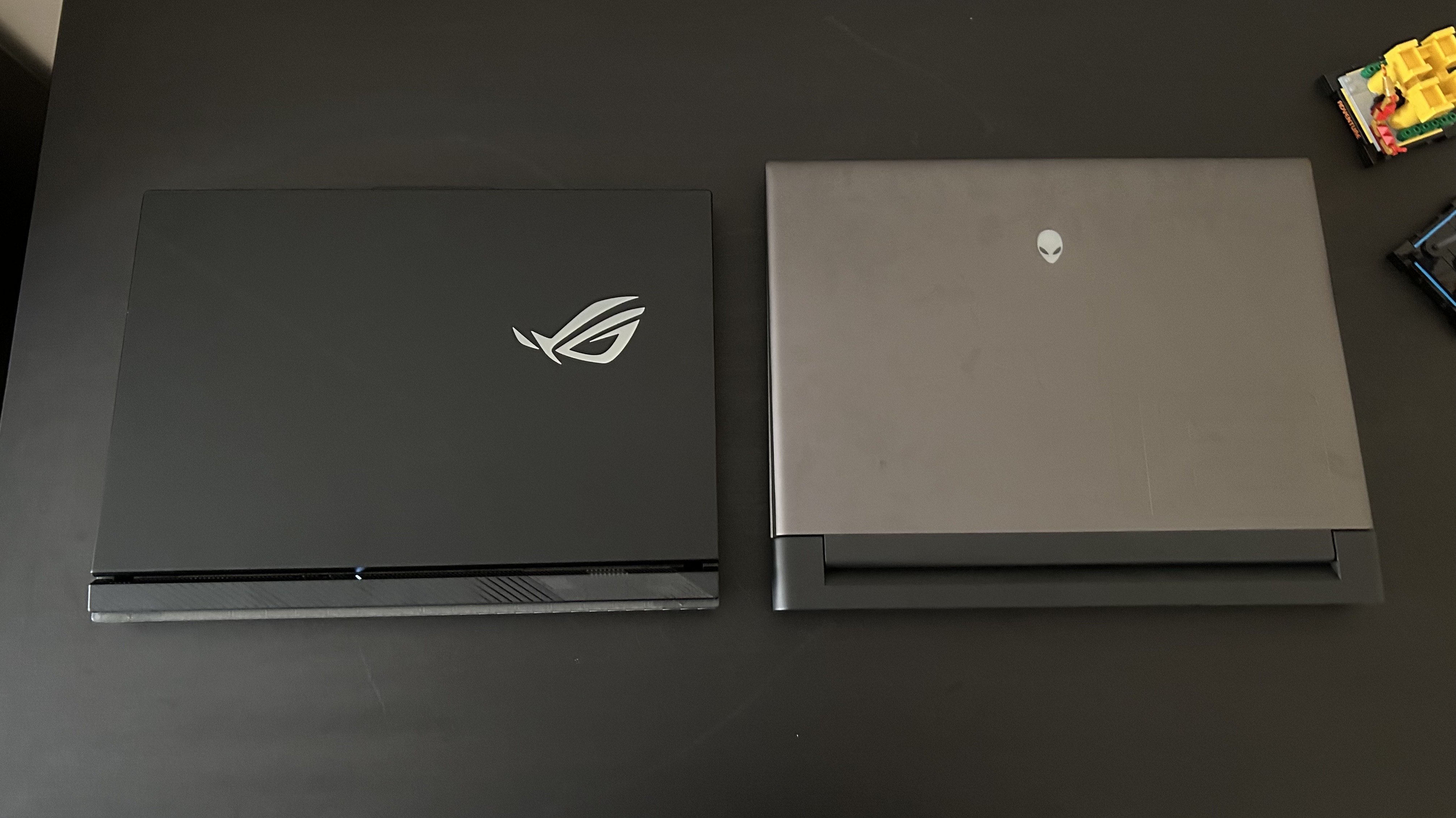 Notebooky Alienware M18 a Asus ROG Strix Scar 18 na černém stole se zavřenými víky a vypnutým RGB