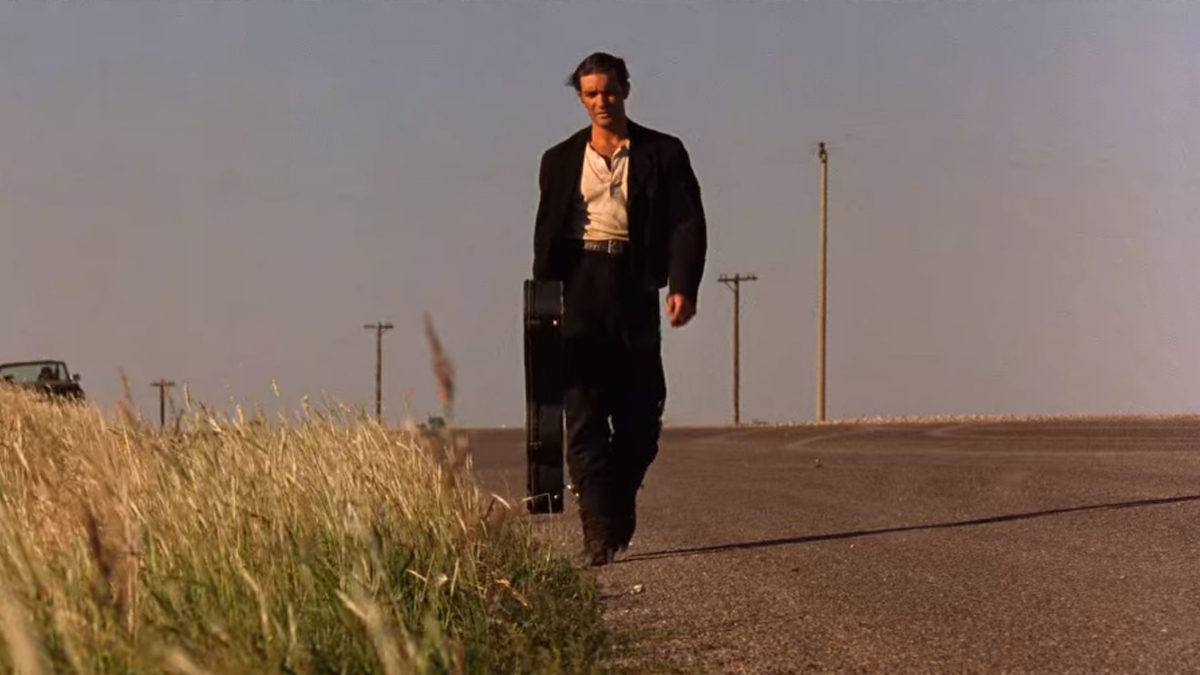 De Mariachi loopt over een woestijnweg met een gitaarkoffer in Desperado