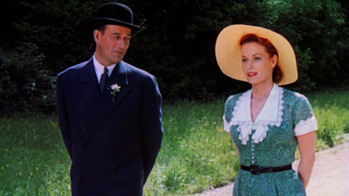John Wayne e Maureen O'Hara caminham num verdejante campo irlandês com roupas dos anos 20 em The Quiet Man