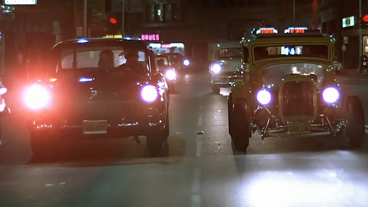 Dos coches hot rod circulan por la calle en la película American Graffiti