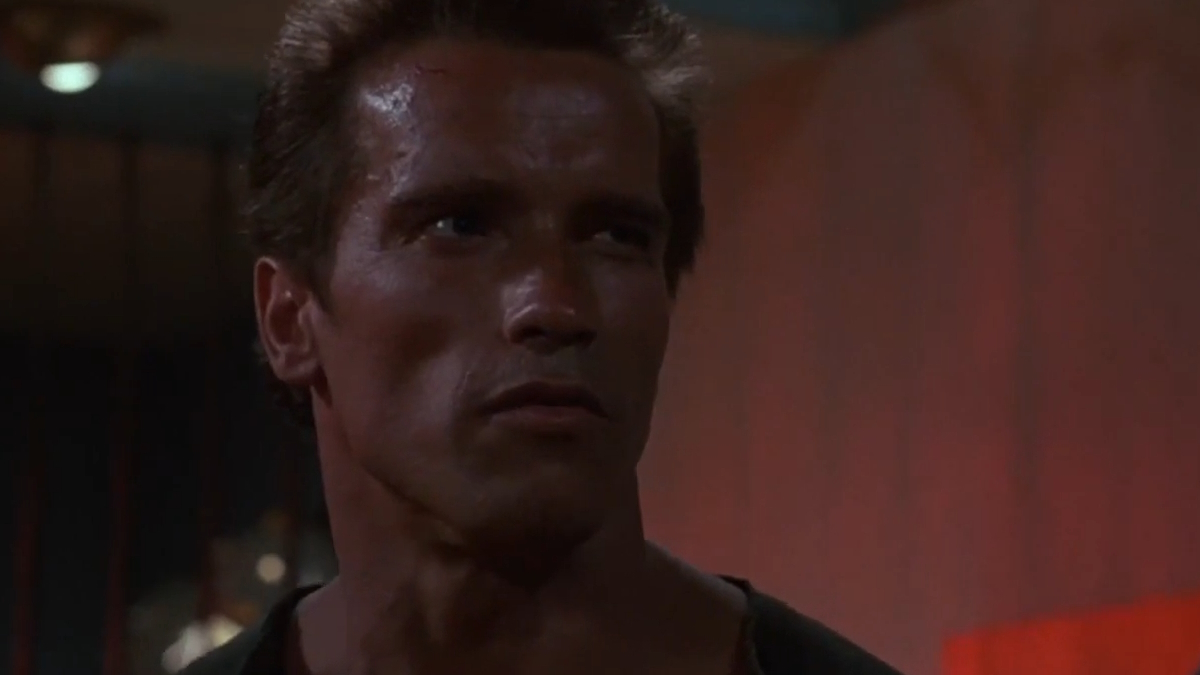 Arnold Schwarzenegger está de pé num quarto de hotel em Commando