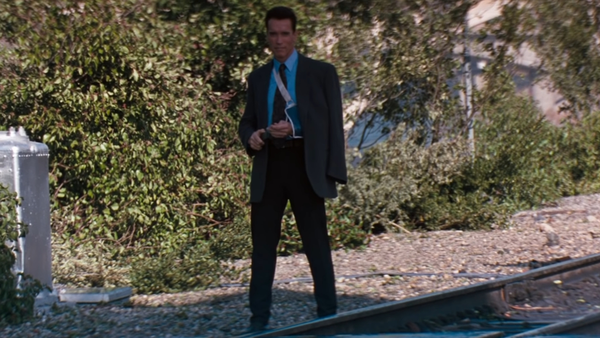 Arnolds Schwarzenegger è in piedi sui binari della ferrovia con in mano un telefono in Eraser
