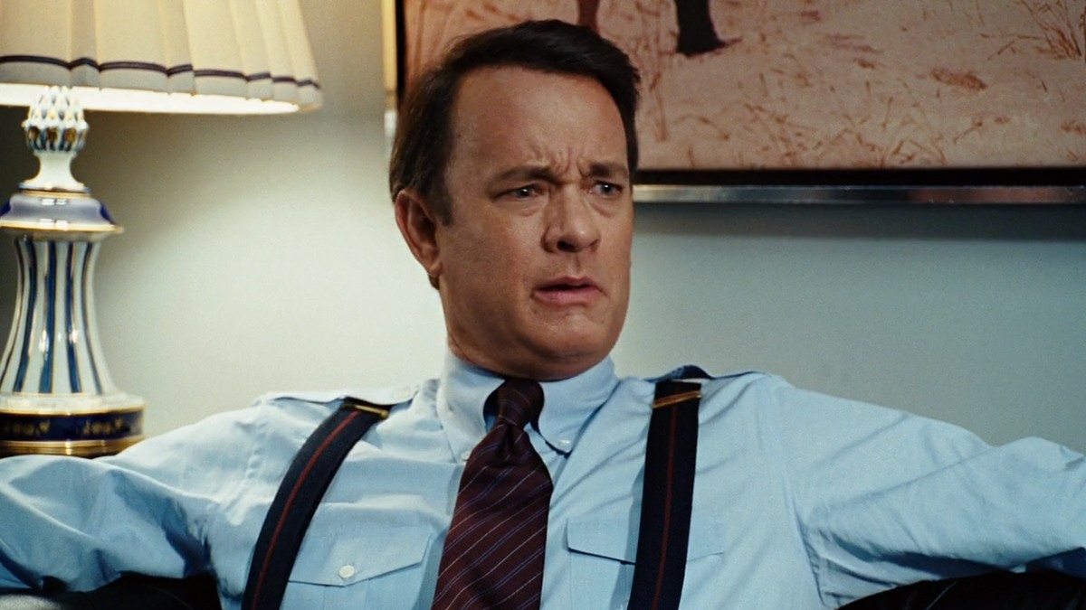 Tom Hanks leží ve své kanceláři a tváří se šokovaně ve filmu Válka Charlieho Wilsona.