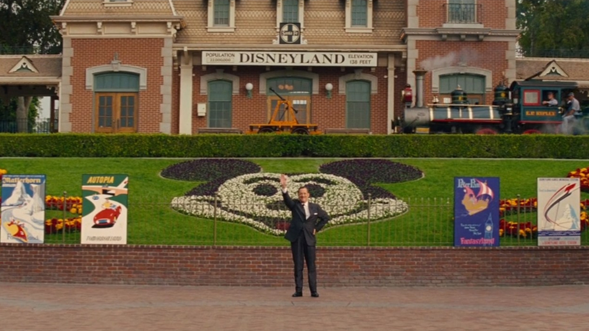 Pan Banks v podání Toma Hankse stojí u brány Disneylandu před zahradou s Mickey Mousem ve filmu Zachraňte pana Bankse.