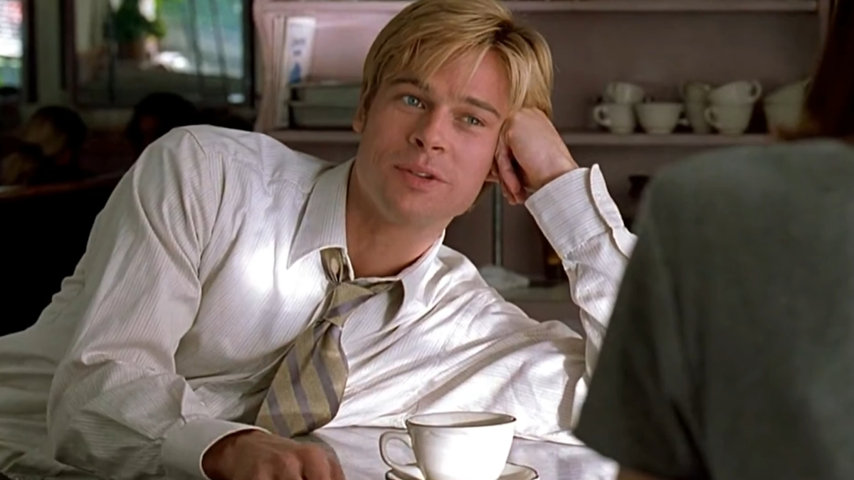 Brad Pitt v košili a kravatě se naklání přes pult, zatímco pije kávu ve filmu Seznamte se, Joe Black