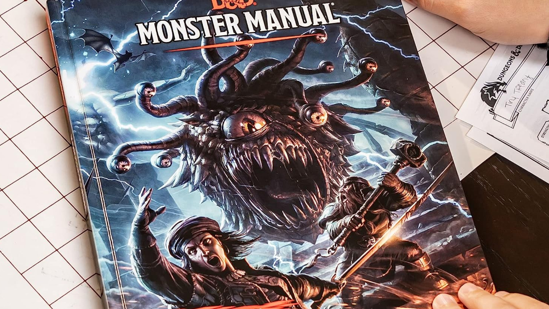 Libro del Manual de Monstruos sobre una mesa y una rejilla