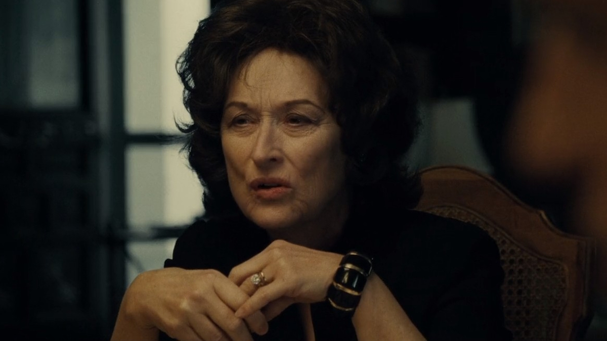 Meryl Streep, jolla on pörröiset mustat hiukset, istuu perheensä ruokapöydässä elokuvassa August: Osage County.