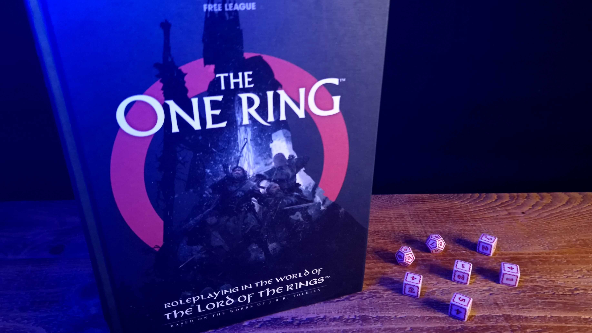 The One Ring Core Rulebook og terninger på et trebord mot en mørk bakgrunn.