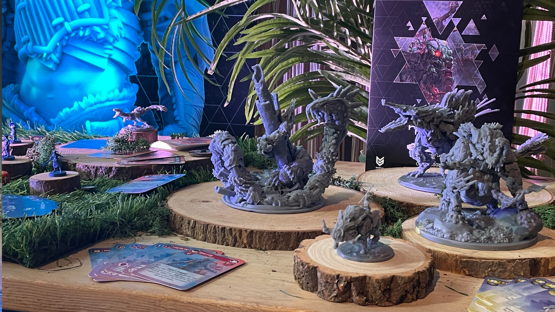 Миниатюры из игры Horizon Forbidden West: Seeds of Rebellion на деревянных кругах на столе, с растительностью на заднем плане