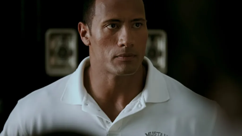 Dwayne Johnson fehér pólóban futballedzőként egy sportöltözőben