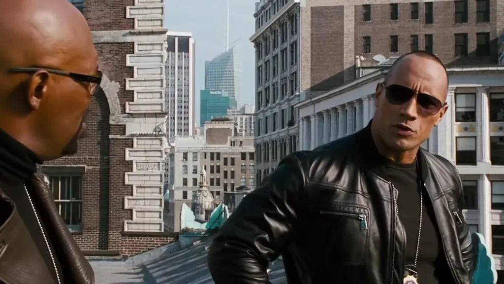 Dwayne Johnson menő napszemüveget és bőrdzsekit viselve mosolyog a NYPD-s partnerére a The Other Guys-ban