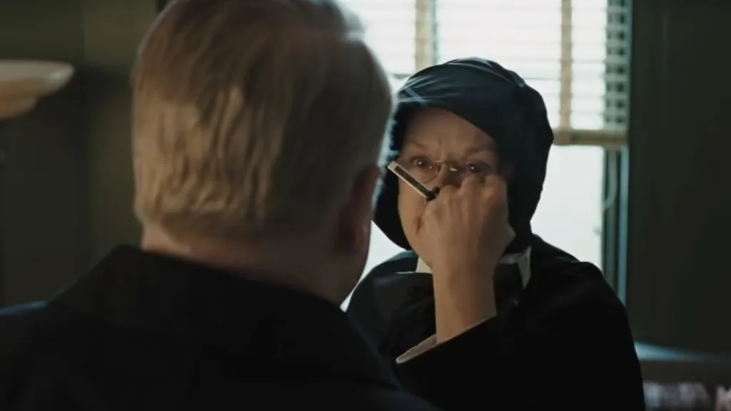 Meryl Streep, mint katolikus apáca, keresztet tart egy pap arcába.